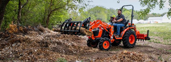 Kubota B Series compact tractor with a grapple attachment clearing brush