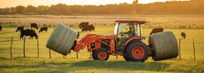 Kubota Grand L70 Series tractor moving round bales in a cattle pasture