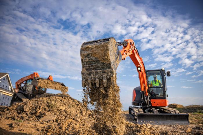 Kubota KX057-5 compact excavator dumping a bucket of dirt on a job site