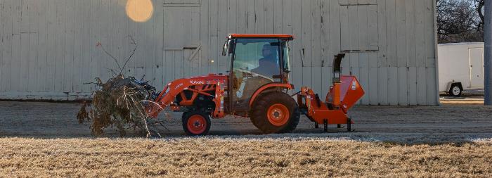 Kubota LX Series compact tractor with a cab, loader, and wood chipper attachment