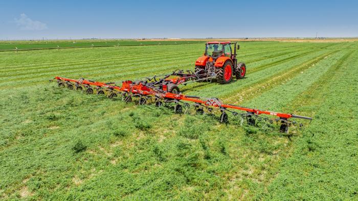 Kubota tractor towing a TE Series tedder through an alfalfa field